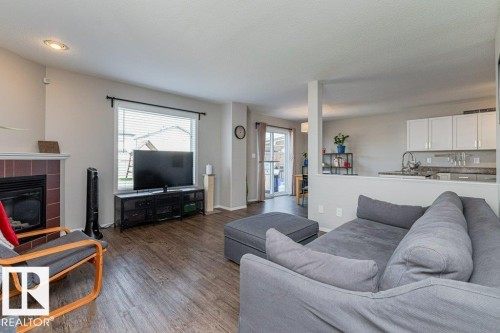Open-concept living area featuring wood-finish flooring, a fireplace with a tiled surround, a large window with blinds, and recessed lighting - 1816 36 Avenue, Edmonton, AB 