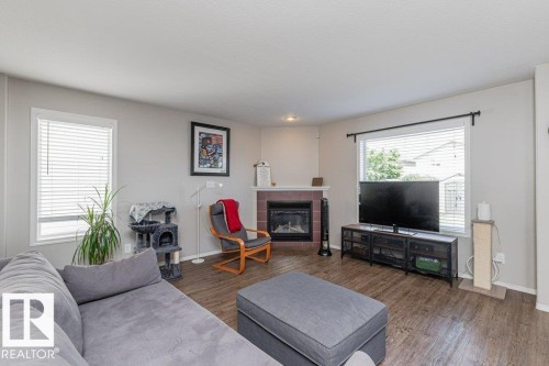 Living area featuring wood-finish flooring, a corner fireplace with a dark red tile surround and white mantel, and multiple windows with white blinds - 1816 36 Avenue, Edmonton, AB 