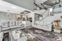 Open-concept living space featuring a modern kitchen with a large island, wood-finish flooring, and a contemporary glass railing staircase - 