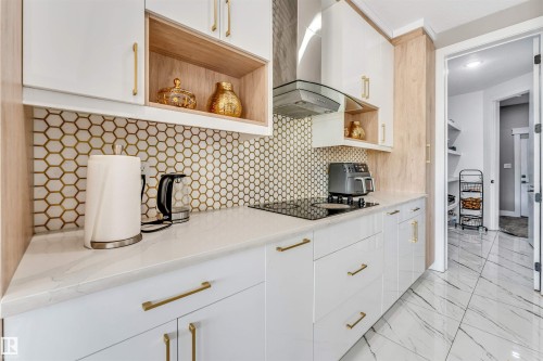 Modern kitchen featuring a white and natural wood-finish cabinetry, a geometric tile backsplash, white countertops, an integrated cooktop, and a stainless steel range hood - 715 Ebbers Place Nw, Edmonton, AB 