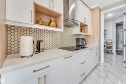 Modern kitchen featuring a white and natural wood-finish cabinetry, a geometric tile backsplash, white countertops, an integrated cooktop, and a stainless steel range hood - 