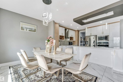 Open-concept dining area and kitchen featuring marble-finish flooring and a contemporary chandelier - 715 Ebbers Place Nw, Edmonton, AB 