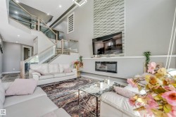 Great room featuring high ceilings, a contemporary fireplace, a decorative wall panel accent, recessed lighting, and a modern glass and wood-finish railing staircase - 