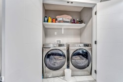 Dedicated laundry closet featuring a built-in shelf, two front-loading appliances, and a marble-look tile floor - 