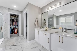 Spacious bathroom featuring a dual vanity with white cabinetry and gold-tone hardware, large rectangular mirror, and white tile flooring - 