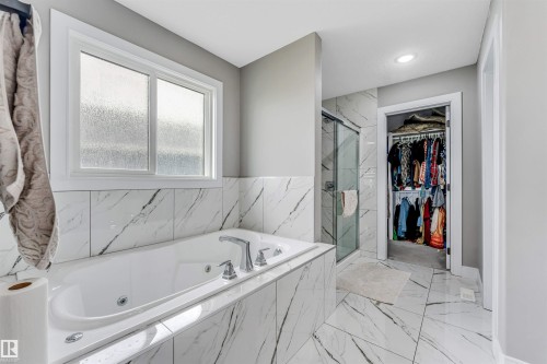 Spacious bath featuring a built-in jetted tub with polished chrome fixtures, white-framed privacy window, and large format marble-look tile flooring and tub surround - 715 Ebbers Place Nw, Edmonton, AB 