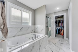 Spacious bath featuring a built-in jetted tub with polished chrome fixtures, white-framed privacy window, and large format marble-look tile flooring and tub surround - 