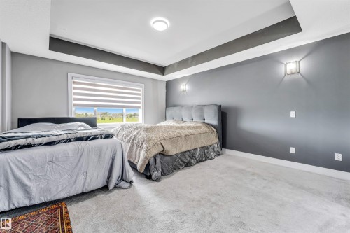 Carpeted room featuring a large window with horizontal blinds, tray ceiling, and wall-mounted sconces - 715 Ebbers Place Nw, Edmonton, AB 