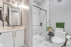 Bathroom featuring a white vanity with a light-toned countertop, a framed rectangular mirror, and a shower with a sliding glass door - 