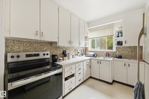 Kitchen featuring white cabinetry, tile backsplash, built-in sink, and a window - 11325 101 Street, Edmonton, AB 