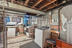 Utility space featuring exposed ceiling joists, concrete flooring, a top-loading washing machine, and electrical panels - 