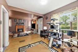 Living area featuring wood-finish flooring, a decorative fireplace with wood surround, and a large window providing natural light - 