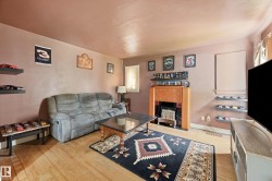 Warm-toned interior featuring wood-finish flooring, a traditional fireplace with a wood surround, and multiple wall-mounted floating shelves - 