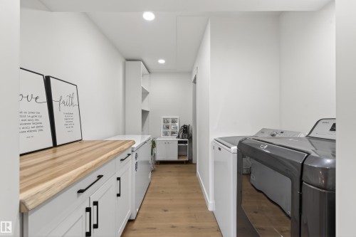 Functional utility room featuring wood-finish flooring, recessed lighting, and white cabinetry with black hardware - 711 Beach Avenue, Cold Lake, AB - Indoor Photo Showing Laundry Room