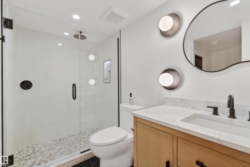Modern bathroom featuring a glass-enclosed shower with a rainfall showerhead, pebble tile flooring, and a recessed niche - 711 Beach Avenue, Cold Lake, AB - Indoor Photo Showing Bathroom