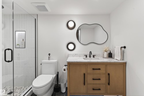 Contemporary bathroom featuring a light wood-finish vanity with black hardware, a quartz-finish countertop, and a uniquely shaped wall mirror - 711 Beach Avenue, Cold Lake, AB - Indoor Photo Showing Bathroom