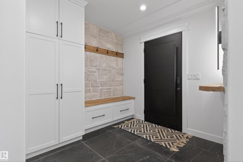 Entryway featuring a modern black door, built-in white cabinetry, a stone accent wall, a wood-finish bench with storage, and dark tile flooring - 711 Beach Avenue, Cold Lake, AB - Indoor Photo Showing Other Room