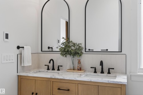 Dual arched mirrors with black frames complement the light wood-finish vanity featuring a stone countertop and integrated sinks - 711 Beach Avenue, Cold Lake, AB - Indoor Photo Showing Bathroom