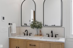 Dual arched mirrors with black frames complement the light wood-finish vanity featuring a stone countertop and integrated sinks - 