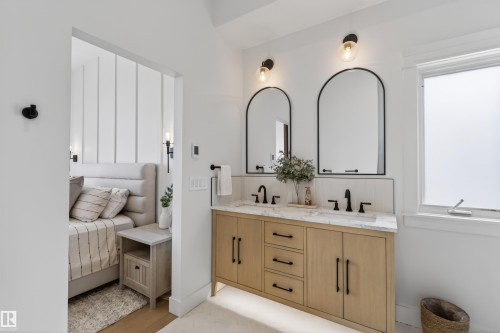 Double vanity with wood-finish cabinetry, quartz countertop, and dual arched mirrors with matte black sconce lighting - 711 Beach Avenue, Cold Lake, AB - Indoor Photo Showing Bathroom
