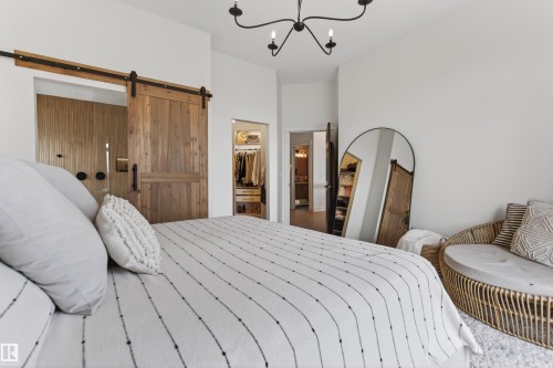 Spacious room featuring a rustic wood barn door, recessed lighting, and a modern chandelier - 711 Beach Avenue, Cold Lake, AB - Indoor Photo Showing Bedroom