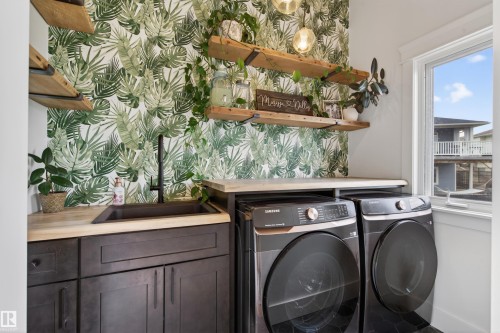Laundry area featuring a built-in dark cabinetry with integrated sink, wood-finish countertops, open shelving, and a patterned accent wall - 711 Beach Avenue, Cold Lake, AB - Indoor Photo Showing Laundry Room