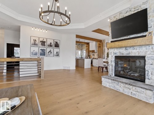Spacious living area featuring light wood-finish flooring, a stone-clad fireplace with a natural wood mantel, and a tray ceiling with crown molding - 711 Beach Avenue, Cold Lake, AB - Indoor Photo Showing Living Room With Fireplace