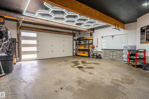 Garage featuring a modern white overhead door with horizontal frosted glass inserts, exposed wood ceiling beams, and contemporary hexagonal ceiling lighting - 711 Beach Avenue, Cold Lake, AB - Indoor Photo Showing Garage
