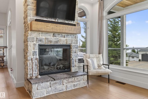 Stone-clad fireplace featuring a rustic wood mantel and a glass-front firebox - 711 Beach Avenue, Cold Lake, AB - Indoor Photo Showing Living Room With Fireplace