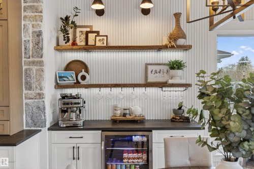 Custom beverage bar featuring white shaker cabinetry, dark countertops, a built-in beverage refrigerator, wood-finish floating shelves with integrated lighting, and vertical plank wall paneling - 711 Beach Avenue, Cold Lake, AB - Indoor