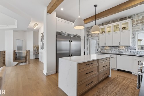 Gourmet kitchen with stainless steel refrigerator, stone accent wall, white cabinetry with display features, substantial island with wood-finish drawers, and two pendant light fixtures - 711 Beach Avenue, Cold Lake, AB - Indoor Photo Showing Kitchen With Upgraded Kitchen