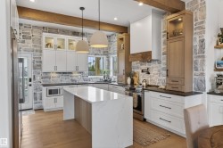 Gourmet kitchen featuring stone accent walls, wood-finish flooring, a central island with a waterfall countertop, white cabinetry with glass display fronts, and a built-in microwave - 
