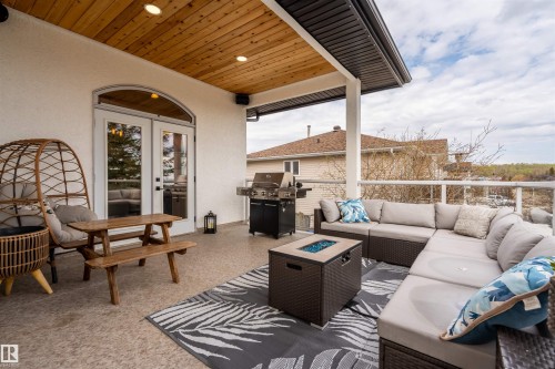 Spacious outdoor patio featuring a wood-panel ceiling with recessed lighting, an arched double-door entry, a built-in outdoor grill, a glass panel railing, and a patterned area rug - 711 Beach Avenue, Cold Lake, AB - Outdoor With Deck Patio Veranda With Exterior