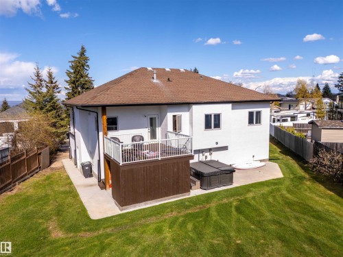 Rear exterior featuring a brown shingle roof, white siding, and a wooden deck with glass railings - 711 Beach Avenue, Cold Lake, AB - Outdoor With Deck Patio Veranda