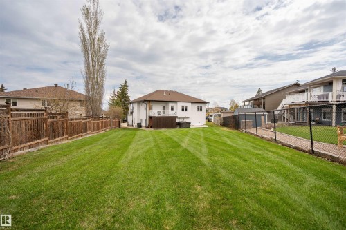 Expansive backyard featuring a lush green lawn, full wood privacy fence, and a white exterior residence with a brown shingle roof - 711 Beach Avenue, Cold Lake, AB - Outdoor With Deck Patio Veranda With Backyard