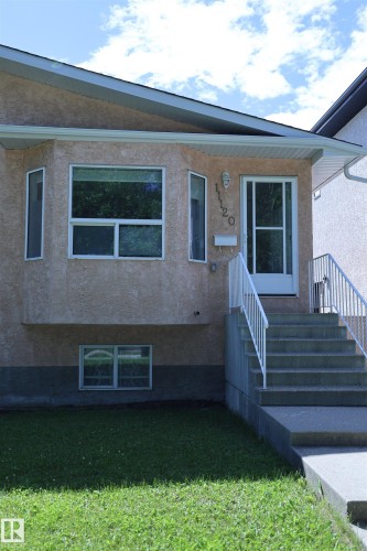 Stucco exterior with a bay window feature, white-framed windows, and a concrete staircase with white railings leading to the main entrance - 11120 132 Street, Edmonton, AB 