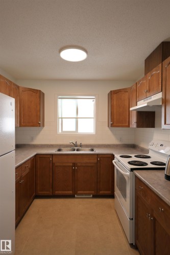 U-shaped kitchen featuring wood cabinetry, a double basin stainless steel sink, and light-toned countertops - 11120 132 Street, Edmonton, AB 