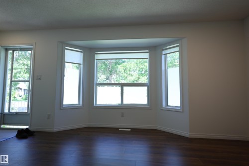 Spacious room featuring a bay window, wood-finish flooring, white walls, and white trim - 11120 132 Street, Edmonton, AB 