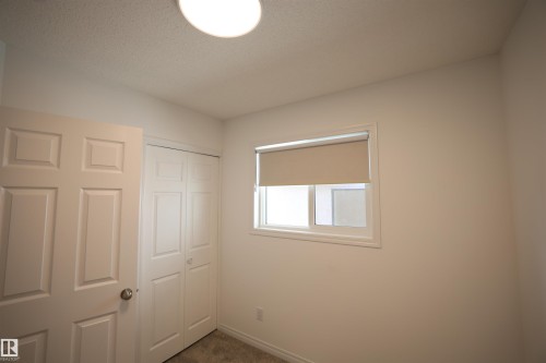 Room featuring white walls, a white paneled door, bi-fold closet doors, a white-framed window with a roller shade, and a flush-mount ceiling light fixture - 11120 132 Street, Edmonton, AB 