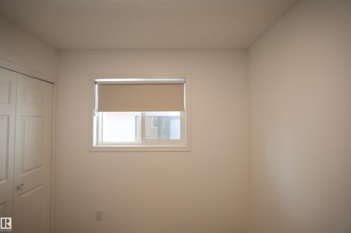 Neutral interior room featuring a window with a roller shade, white trim, and a white paneled bi-fold door - 11120 132 Street, Edmonton, AB 