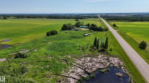 Expansive rural property featuring a long, straight paved road, broad green fields, and a cluster of buildings - Rural Athabasca County, AB 