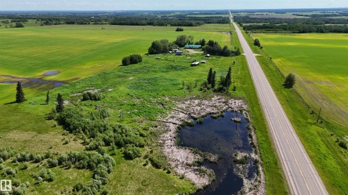 Expansive agricultural property featuring a paved road, cultivated fields, forested areas, a natural pond, and multiple structures - Rural Athabasca County, AB 