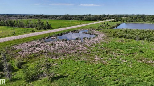 Expansive green land featuring a paved road, natural ponds, and abundant foliage - Rural Athabasca County, AB 