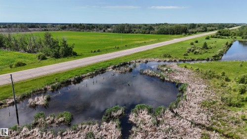 Expansive rural landscape featuring a paved road, open green fields, natural wetlands, and distant treelines under a clear sky - Rural Athabasca County, AB 