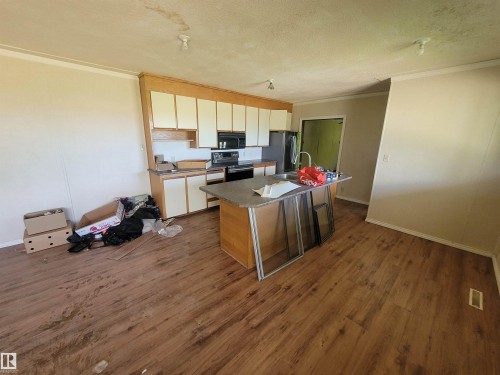 Kitchen featuring wood-finish flooring, a central island with a sink, and perimeter cabinetry with a built-in microwave - Rural Athabasca County, AB 