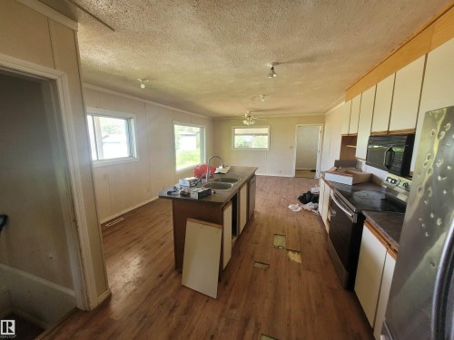 Open-concept kitchen and living area featuring wood-finish flooring, white paneled walls, and multiple windows - Rural Athabasca County, AB 