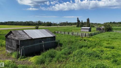 Expansive green landscape featuring multiple outbuildings, a wooden fence, and a paved road in the distance - Rural Athabasca County, AB 