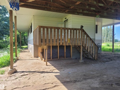 Covered outdoor area featuring a wood deck with stairs, white siding exterior, and exposed concrete foundation - Rural Athabasca County, AB 