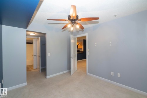 Bedroom featuring neutral carpet flooring, a ceiling fan with wood-finish blades, and light gray walls - 208 3719 Whitelaw Lane, Edmonton, AB 