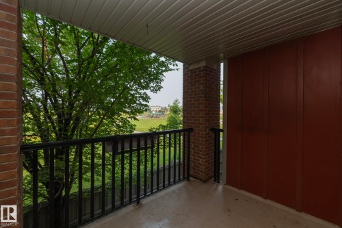 Covered balcony featuring a concrete floor, black metal railing, and brick column - 208 3719 Whitelaw Lane, Edmonton, AB 